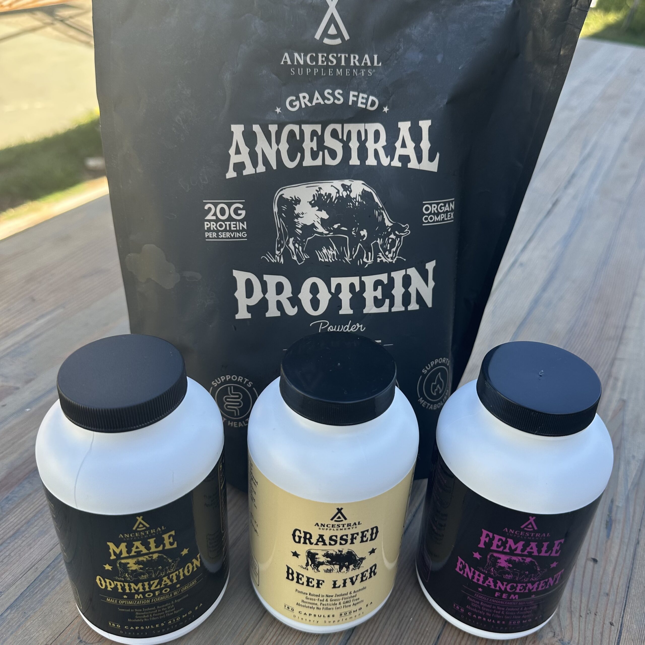 A bag of Ancestral Supplements chocolate protein powder behind three bottles of capsules: MOFO, grass-fed beef liver and FEM